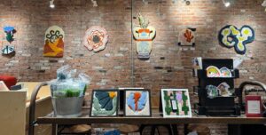 Several fiber arts pieces, hanging on the wall and placed on a shelf.